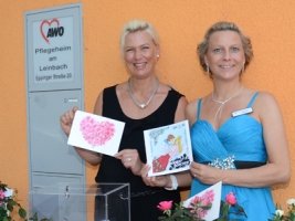 Zwei Frauen halten selbstgemachte Karten in die Luft am Rosenfest Pflegeheim am Leinbach
